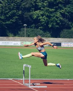 a woman is jumping over a hurdle on a track