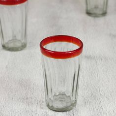 three red rimmed glasses sitting on top of a white tablecloth covered floor next to each other