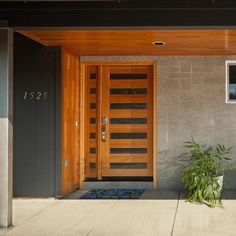 an entrance to a modern home with wood paneling and glass door, plants in the foreground