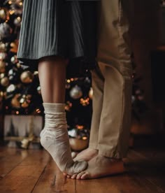 two people standing next to each other with their feet on the ground near a christmas tree