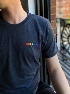 a man sitting on a window sill wearing a black shirt with rainbow letters on it