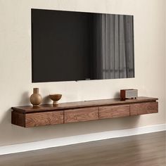 a tv mounted to the side of a wall next to a wooden shelf with two vases on it