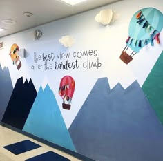 an office wall painted with hot air balloons, mountains and clouds that say it's best view comes after the kindest climb