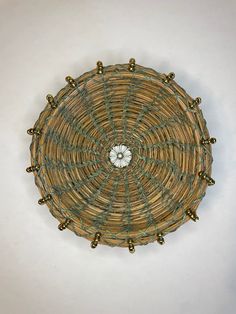 a round woven basket with gold beads on the bottom and green stringing around it