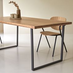 a wooden table with two chairs and a vase on it, in front of a white wall