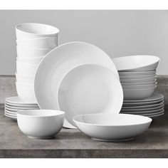 a stack of white dishes sitting on top of a wooden table next to each other