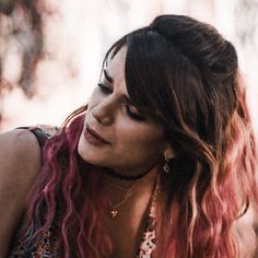 a woman with pink hair and necklaces on her neck looking off to the side