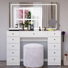 a white dressing table with a mirror and stool in front of it, next to a window