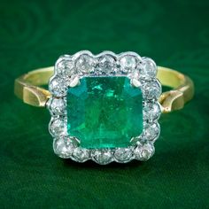 A striking vintage cluster ring built around a natural step cut emerald at its heart, weighing approx. 3.65 carats. It has an intense, vivid green hue and is bordered by sixteen twinkling old mine cut diamonds with SI1 clarity - I colour (approx. 0.80ct total).  Emerald is the birthstone of May. The Romans considered it to be the sacred stone of the goddess Venus and was said to preserve love and provide hope. Its natural green colouring also makes it a stone of springtime and is associated with Vintage Green Emerald Ring Gia Certified, Heirloom Green Cluster Ring, Vintage Green Emerald Ring With Brilliant Cut, Classic Green Cluster Emerald Ring, Antique Green Emerald Cut Emerald Ring, Antique Emerald Cut Green Emerald Ring, Antique Green Emerald Cut Ring, Antique Green Emerald-cut Emerald Ring, Green Emerald Cluster Ring With Center Stone