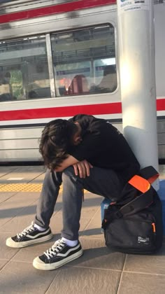 a man sitting on the ground with his head in his hands next to a train