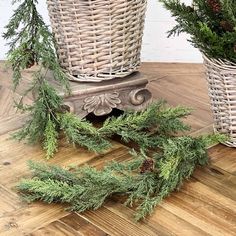 two wicker baskets with evergreen branches and pine cones in them on a wooden floor