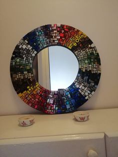 a round mirror sitting on top of a dresser next to a cup and saucer