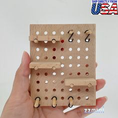 a hand holding a wooden peg board with holes in it and hooks on each side