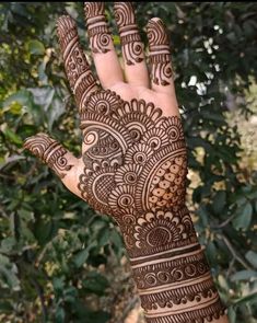 a hand with henna tattoos on it in front of some trees and bushes,