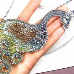 "This necklace was made a showpiece for the annual fair here in San Diego...it it large, gem-encrusted and not for the faint of heart! A fabulous hand-shaped peacock has been formed from various gauges of fine silver wire and meticulous wrapped together. The bird has been filled in with a plethora of varied gemstones: at his head are BLACK DIAMOND chips in his beak, BLACK SPINEL and MOONSTONE around his eye and his neck stretches out, populated with rich blue LONDON BLUE TOPAZ. At the crest of h Wire Wrapped Pendant Jewelry For Parties, Party Wire Wrapped Pendant Jewelry, Handmade Silver-plated Wire Necklaces, Handmade Silver Plated Wire Necklaces, Whimsical Pendant Jewelry For Party, Unique Handmade Silver-plated Wire Jewelry, Unique Silver-plated Wire-wrapped Jewelry, Peacock Design Jewelry Gift, Bohemian Peacock Necklace As Gift