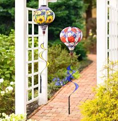 two hot air balloons hanging from the side of a white pergolated arbor in a garden