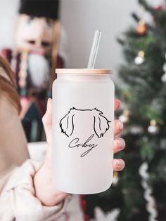 a person holding up a cup with a straw in it and a christmas tree in the background