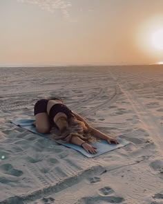 a woman laying on top of a yoga mat in the sand