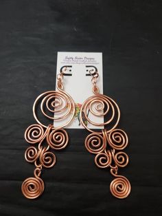 copper earrings with spiral design on black background and white card for sale in the foreground