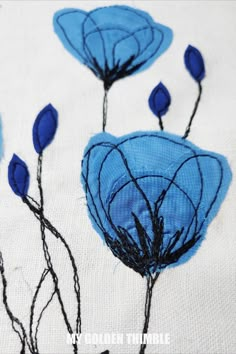 some blue flowers on a white cloth with black stems and leaves in the center, as if they were embroidered onto fabric