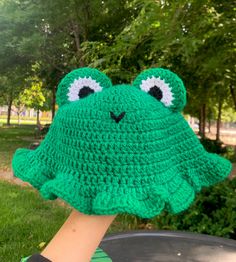 a crocheted frog hat is held up in the air by someone's hand