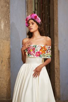 a woman in a white dress with pink flowers on her head standing next to a building