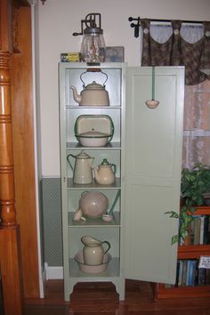 a cabinet with teapots and cups on it next to a bookshelf