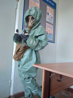 a man in a gas mask and protective suit standing next to a table with a bag on it