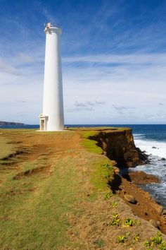 a white lighthouse sitting on top of a cliff next to the ocean with waves coming in