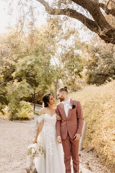 a bride and groom standing in front of a tree at their outdoor wedding ceremony on a dirt path