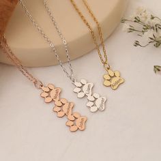 three personalized necklaces on a white surface with flowers in the foreground and a vase behind them