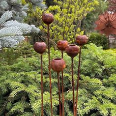 three tall metal flowers in the middle of a garden filled with plants and trees,