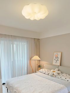 a white bed sitting next to a window in a bedroom under a light fixture and a painting on the wall