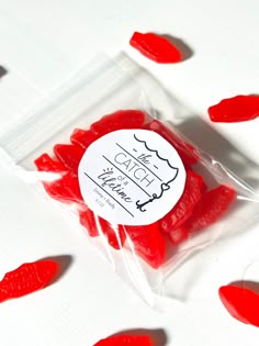 red gummy bears are in a clear bag on a white surface with small hearts scattered around them