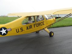 a small yellow airplane sitting on top of an airport tarmac with two people in the cockpit