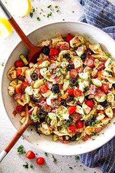 a white bowl filled with pasta salad next to a wooden spoon and lemon wedges