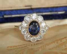 I am thrilled to have acquired this sensational vintage cluster ring for my store. Victorian in style, this piece is graded 'Twentieth Century' by the Guild of Valuers & Jewellers... and I would date this ring as circa 1960. The principal stone is an oval cut natural sapphire surrounded by 10 round brilliant cut diamonds. The sapphire is an impressive 1.06ct and the colour of the stone is graded 'purplish blue', which is a very desirable shade.  The bright, cloudy light was ideal to capture a tr Vintage Cluster Rings Hallmarked, Vintage Blue Sapphire Ring With Halo Setting, Vintage Blue Cluster Ring With Prong Setting, Vintage Brilliant Cut Cluster Diamond Ring, Vintage Sapphire Ring With Halo Setting, Vintage Sapphire Cluster Ring With Gemstones, Vintage Yellow Gold Cluster Ring, Vintage Blue Cluster Ring With Center Stone, Sapphire Cluster Ring With 17 Jewels For Wedding