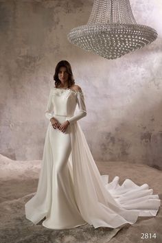 a woman in a white wedding dress standing next to a chandelier and wearing an off - the - shoulder gown