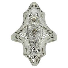 Here we have a delightful Art Deco three-stone diamond ring. Three round faceted old cut diamonds have been individually claw set atop of one another in a vertical fashion amidst a fine milgrain bordering at the centre of the face. This detailing sets the tone of the piece and also dictates the open backdrop design, borrowing from the filigree crafting process. Fleur-de-lis style motifs are neatly nestled within before the ring is finished with a plain polished shank. Condition: Used (Very Good) Stile Art, Stone Diamond Ring, Three Stone Diamond Ring, Platinum Diamond Rings, Three Stone Diamond, Backdrop Design, Platinum Ring, Three Stone Rings, Ring Box