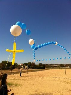 some people are flying kites in the air on a beach with blue and white balloons