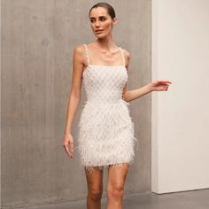 a woman in a short white dress is walking down the runway with her hand on her hip