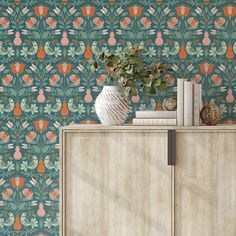 a vase with flowers on top of a wooden cabinet next to a wallpapered background