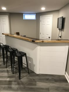 an unfinished basement bar with three stools and a tv mounted on the wall above it