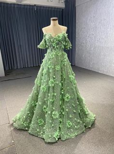 Dappled with intricate floral appliques, this prom dress is designed to captivate and enchant. The serene green color evokes the tranquility of a lush garden, making it an exceptional choice for those who appreciate nature-inspired elegance. The off-the-shoulder neckline enhances your natural grace, while the delicate flowers that adorn the bodice and skirt add a touch of whimsy and romance. The full, flowing skirt is designed to move with you, creating a mesmerizing effect with every step you take. Picture yourself twirling on the dance floor, the soft fabric and intricate details combining to create a look that is both ethereal and unforgettable. This dress is ideal for those who want to blend classic beauty with a fresh, modern twist. Embrace the opportunity to shine in this exquisite g Green Floor-length Wedding Dress For Debutante Ball, Wedding Dress With Long Train For Prom Season Banquet, Long Train Wedding Dress For Banquet And Prom Season, Luxury Wedding Dress With Long Train For Banquet, Green Fitted Ball Gown For Debutante Ball, Fitted Ball Gown With Long Train For Banquet, Green Wedding Dress With Sweep Train, Green Wedding Dress With Sweep Train For Debutante Ball, Wedding Evening Dress With Detachable Train For Prom Season