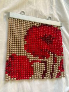 a red and white beaded art piece on top of a white cloth covered bed