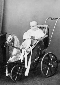 an old black and white photo of a baby sitting in a carriage with a horse