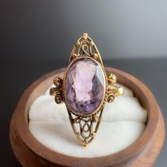 A beautiful 14ct yellow gold art nouveau navette ring featuring an oval cut amethyst bezel set on a decorative marquise shaped ornate delicately detailed with edging and scroll leading to decorative scroll shoulders and a classic domed band. - Marked 585  - The Ring is a UK size T which can be resized. - Approximately 6.10 grams. - Please note before ordering if sizing is selected existing hallmarks are likely to be polished out   We cannot accept any returns if sizing is selected on your order. Oval Amethyst Ring Stamped 14k, Art Deco Amethyst Ring In Yellow Gold, Yellow Gold Amethyst Ring In Art Deco Style, Art Deco Yellow Gold Amethyst Ring, Heirloom Gold Amethyst Ring With Bezel Setting, Collectible Oval Cabochon Amethyst Ring, Oval Amethyst Ring With Bezel Setting For Formal Occasions, 14k Gold Art Deco Amethyst Ring, 14k Gold Amethyst Ring Art Deco Style