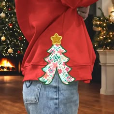 a person wearing a red sweatshirt with a christmas tree applique on the back