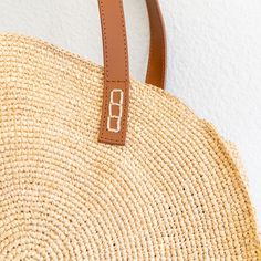 a close up of a straw bag on a white wall with a brown leather handle