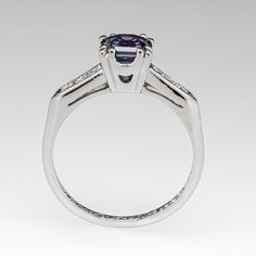 This gorgeous blue to purple color change sapphire engagement ring features a 1.16 carat no heat sapphire with Montana, USA origin that we sourced and set in a vintage platinum diamond mounting. The shoulders of the ring are each accented with three (3), channel set, round single cut diamonds, bordered with milgrain edging. The ring measures 6.2mm at the top, rises 6.3mm above the finger, tapering to 1.5mm wide and 1.3mm thick at the base of the shank. The ring is currently a size 5.75 and we offer complimentary resizing to fit. Classic Sapphire Rings In Purple, Purple Sapphire Ring With Brilliant Cut For Anniversary, Purple Sapphire Ring With Center Stone In Round Cut, Purple Sapphire Ring With Brilliant Cut, Purple Sapphire Ring With Center Stone, Round Cut, Classic Purple Sapphire Promise Ring, Classic Purple Sapphire Ring With Prong Setting, Purple Sapphire Ring With Round Cut And Prong Setting, Purple Sapphire Ring With Prong Setting